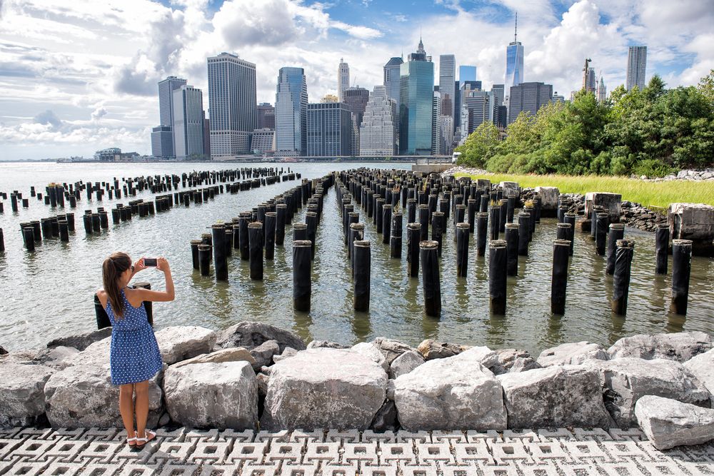 A woman capturing the NY Skyline from Brooklyn Bridge Park