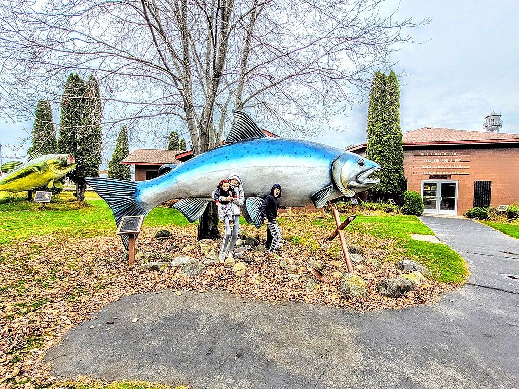 A family posing infront of the salmon statue at Freshwater Fishing Hall of Fame