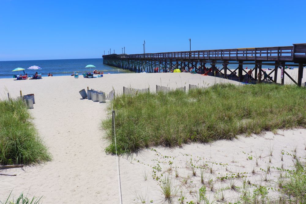 Sand near the body of water and bridge at Holden Beach Pier.