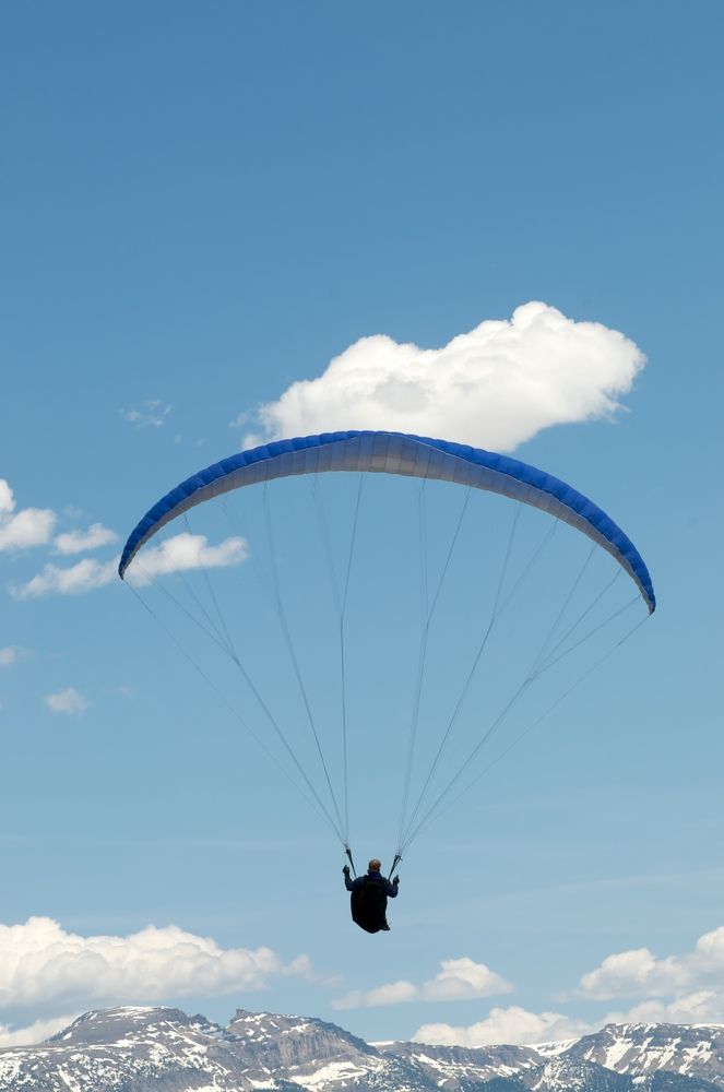 Closer view of a paraglider at Jackson Hole Paragliding with fluffy clouds and mountains in the background