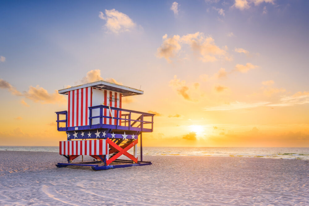 A red, white and blue lifeguard stand on an empty beach at sunrise