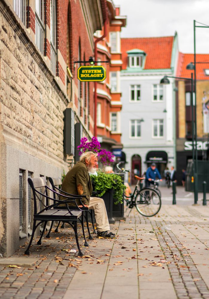 An old man sitting on the sidewalk bench in the old town of Lund