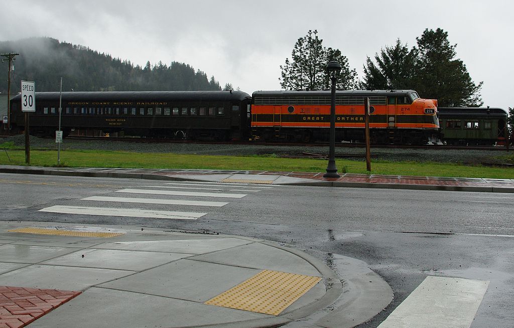 A train passin at a junction on a rainy day with mountains and trees in the background at Oregon