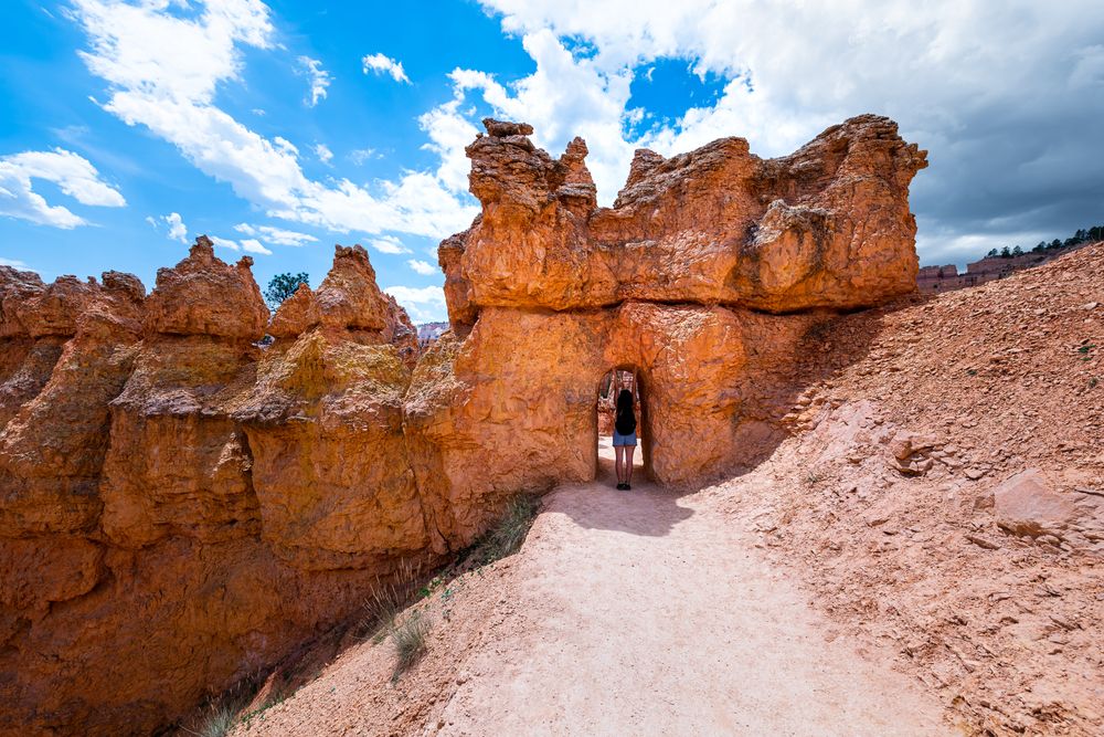 A tourish walking through a natural rock tunnel along the Queens Garden Trail