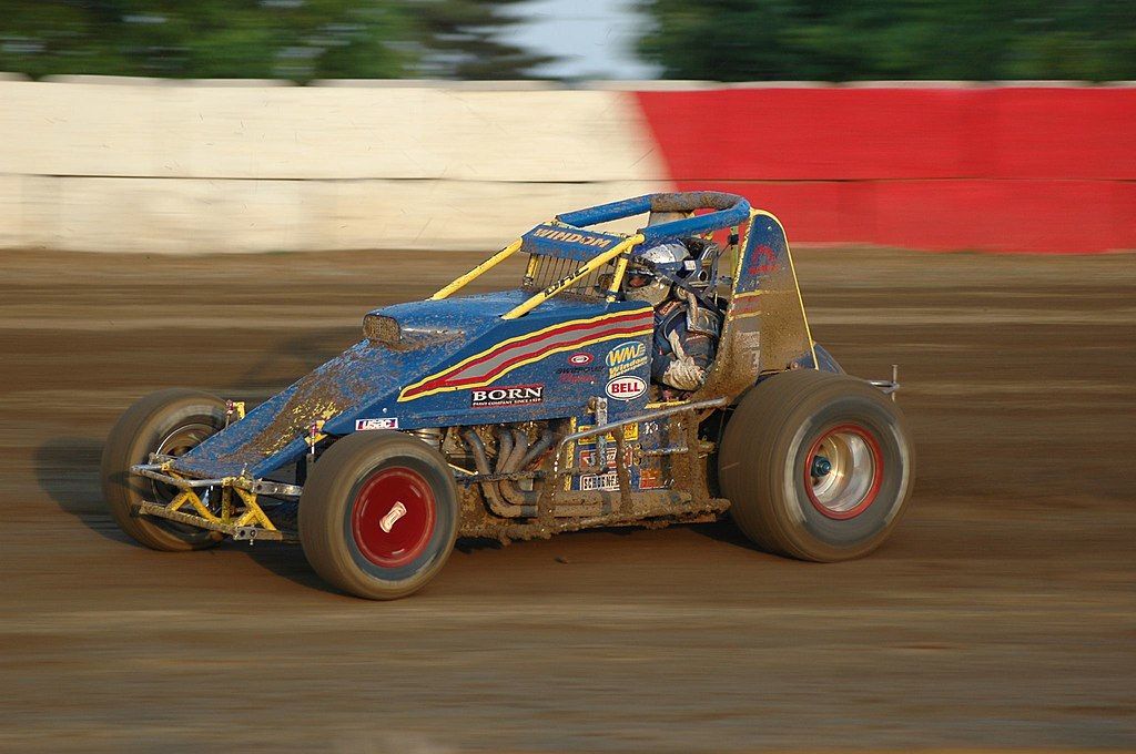 A blue muddy car racing the wind at Terre Haute Action Track