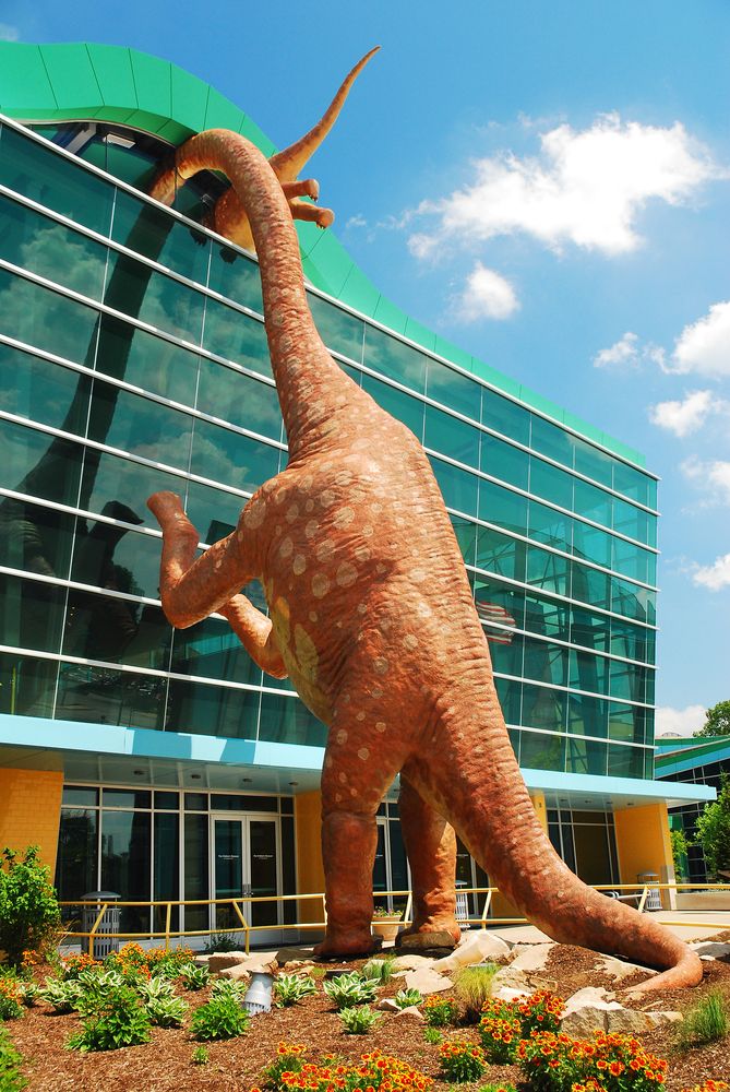 Statue of a dinosaur peeking into The Children's Museum of Indianapolis
