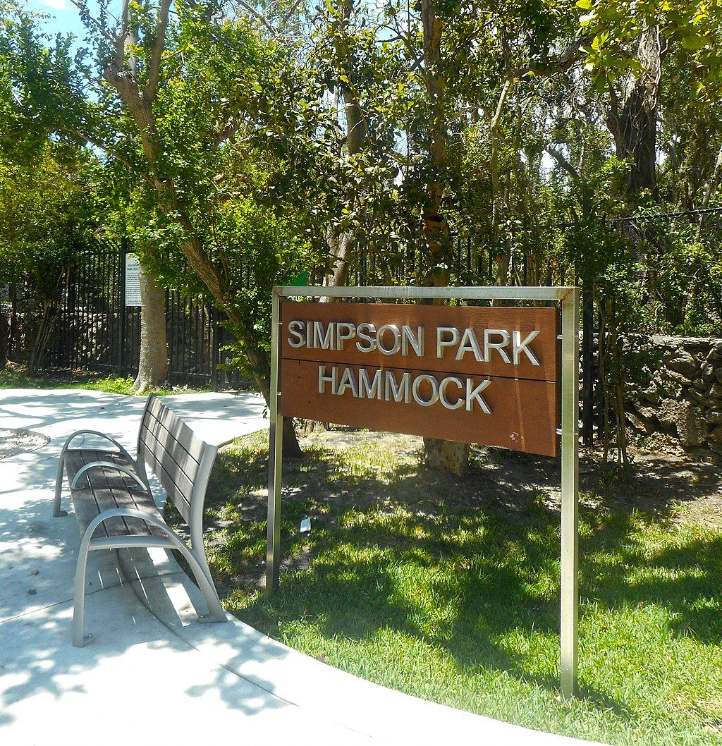 A wooden bench in front of Simpson Park Hammock's welcome sign