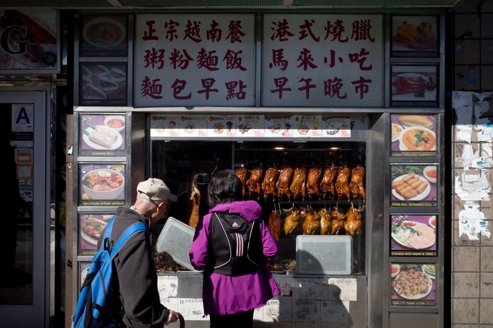 A man and a woman standing in front of a store selling roasted ducks.