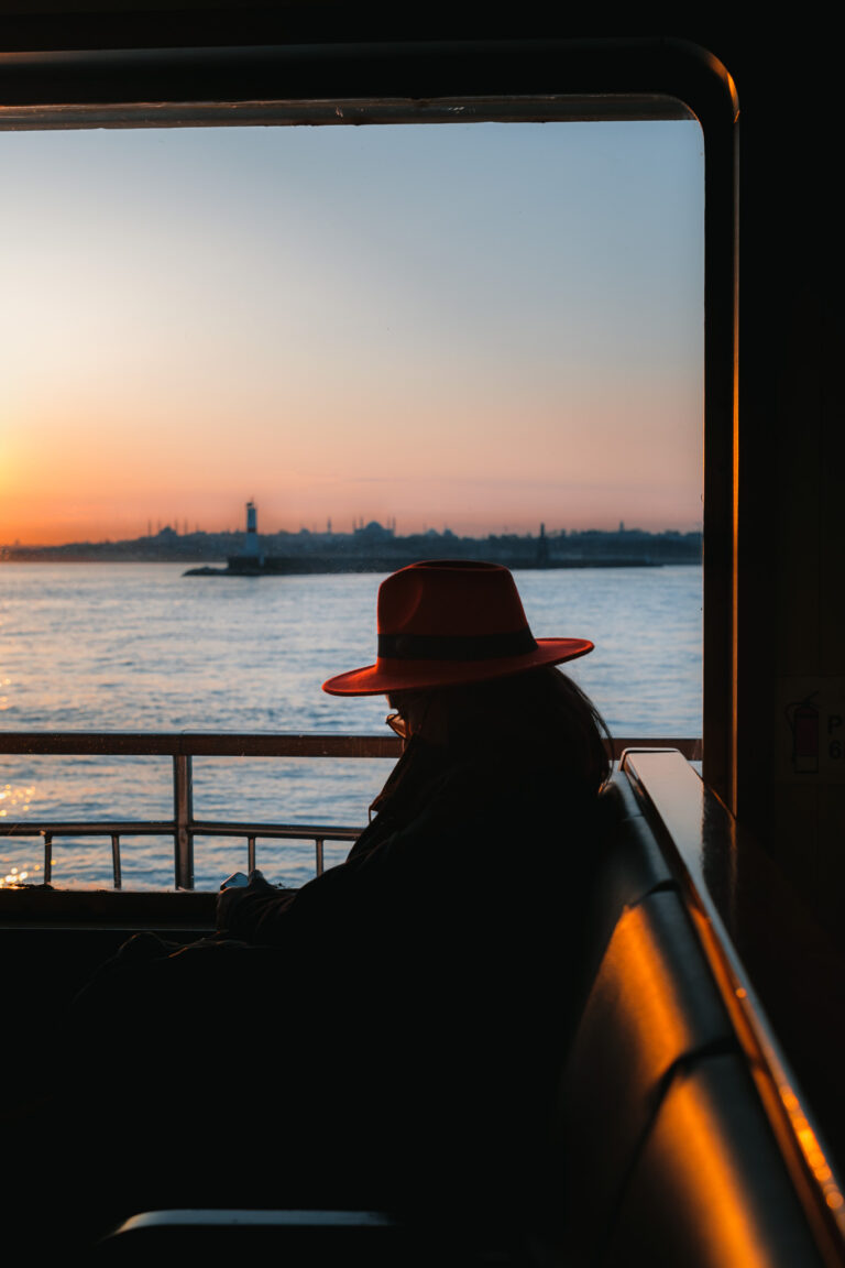 A solitary figure in a striking red hat gazes out at the tranquil waters of Istanbul at sunset