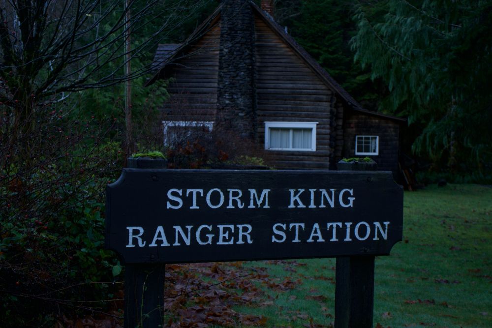Wooden name sign of the storm king ranger station with the house behind it.