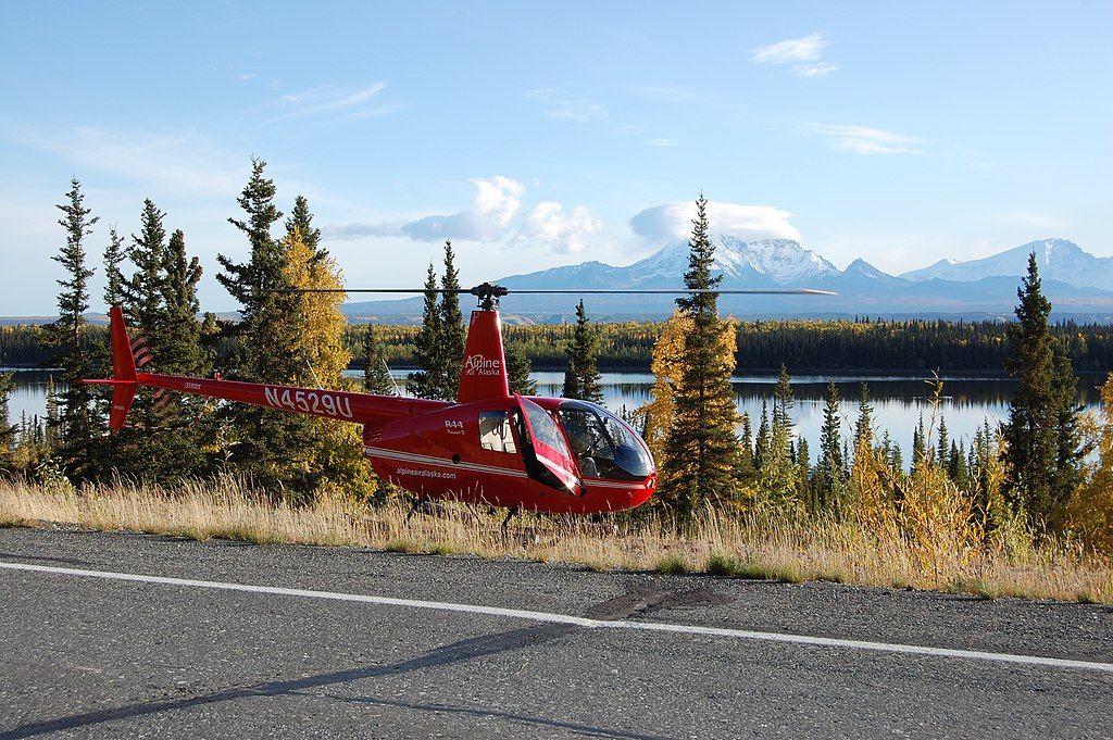 A red helicopter parked near a body of water.