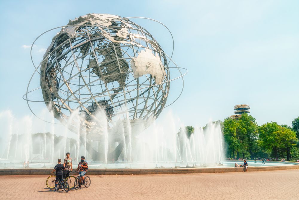 A huge uni-sphere with water fountains surrounding it, and people riding bikes.
