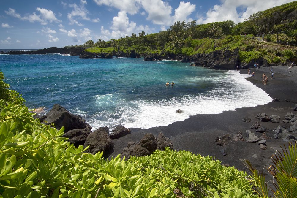 People standing on the black sand of Waianapanapa State Park