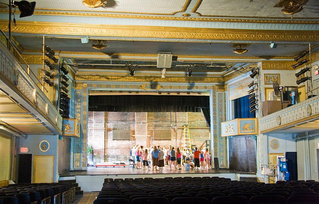 Interior of the apollo theatre with empty audience seats and people rehearsing on stage.