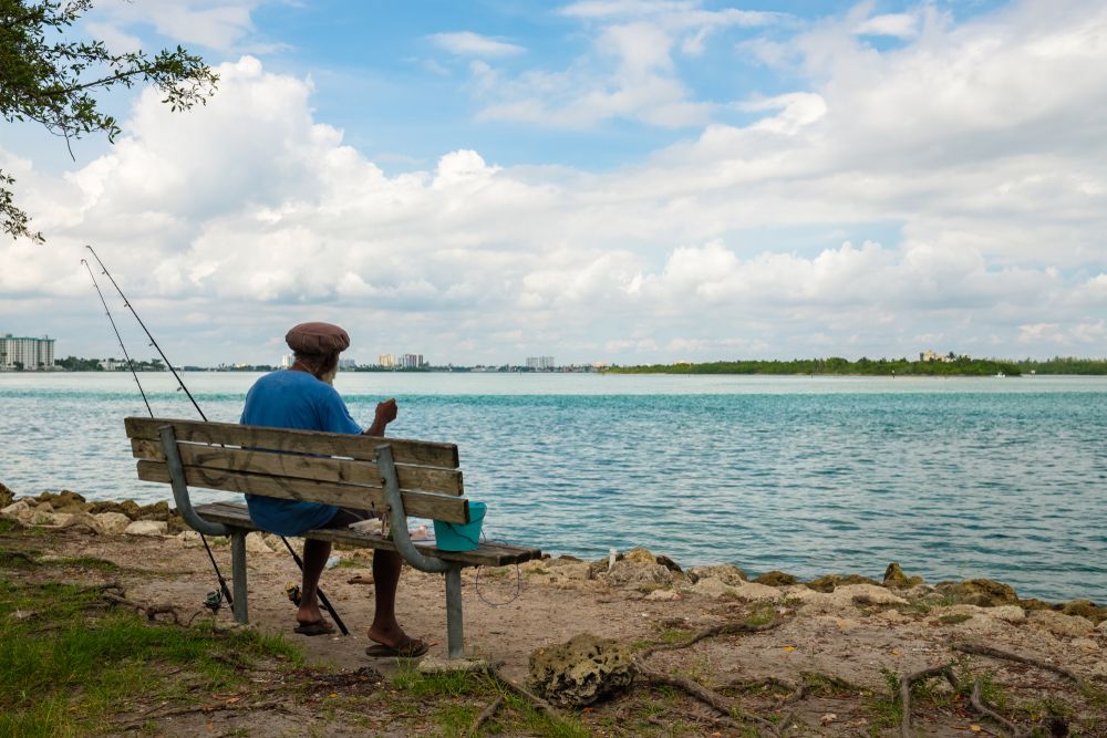 A man sitting on a bench with a fishing rod at Haulover Park Beach