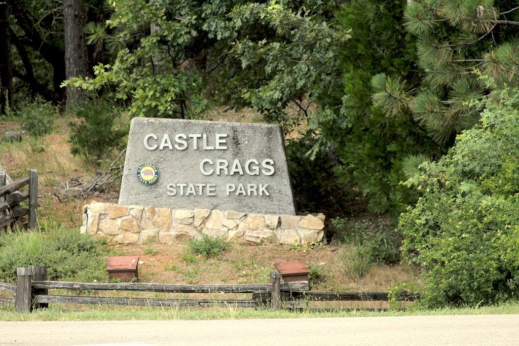 Castle Crags state park welcoming sign with tall green trees at the side.