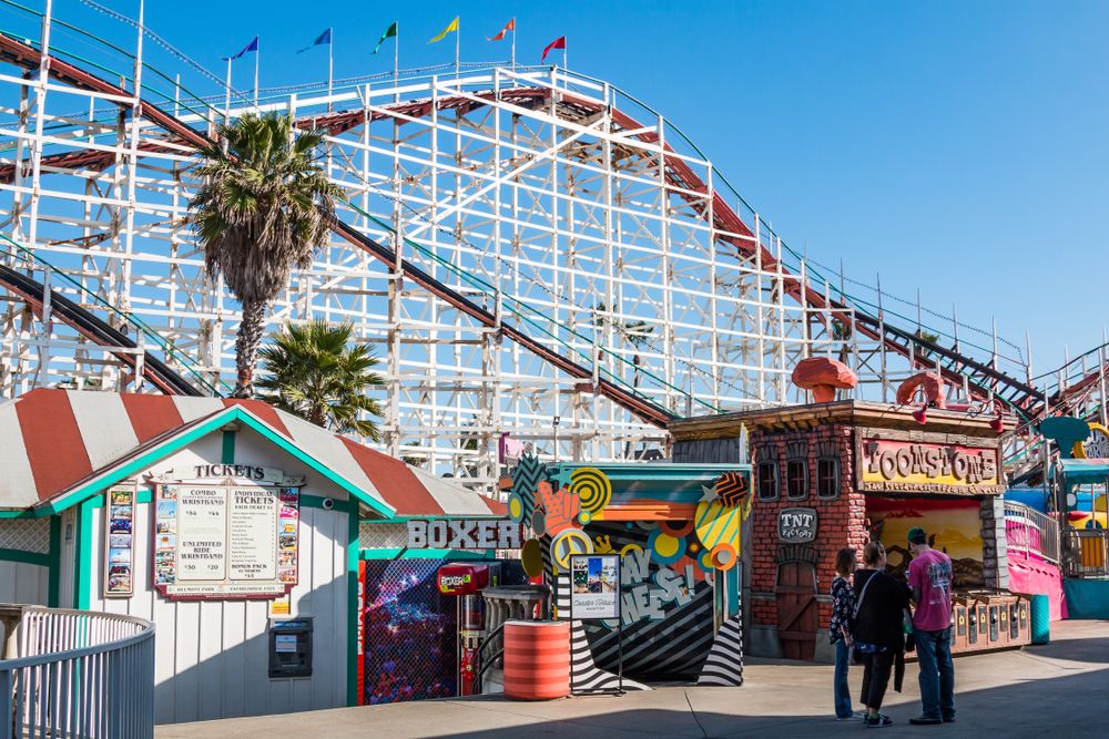 Inside the belmont park with part of a roller coaster behind a ticket booth.