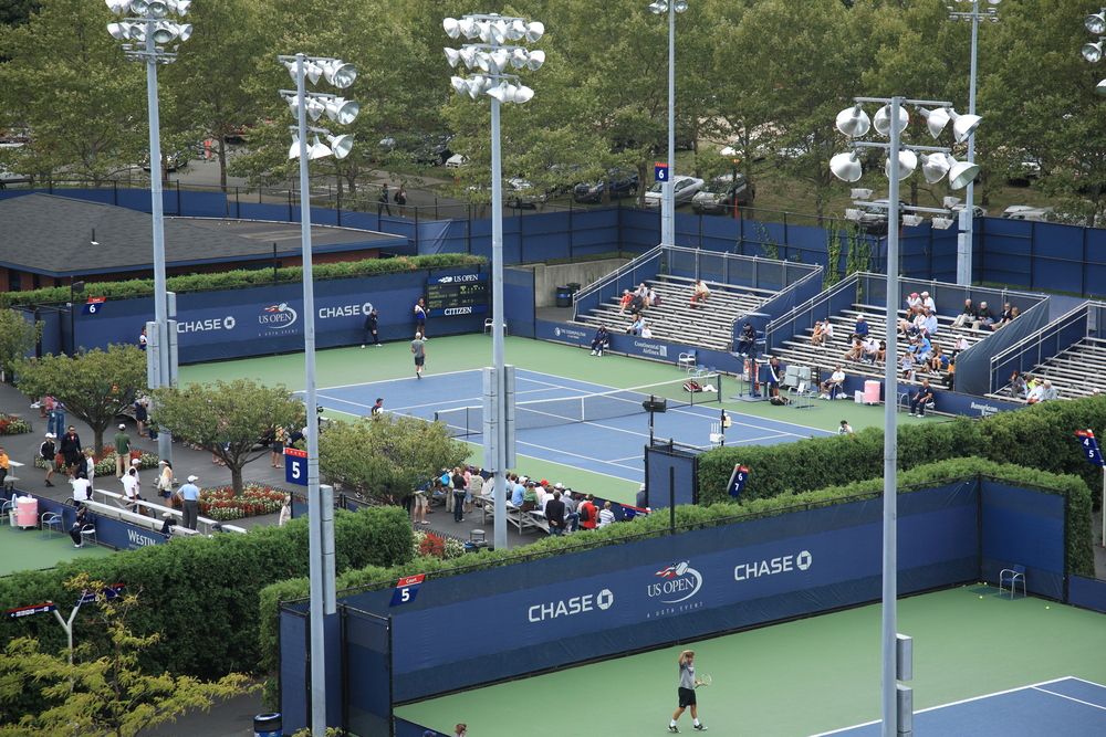 Open tennis court with tall light posts, and people sitting on the benches.