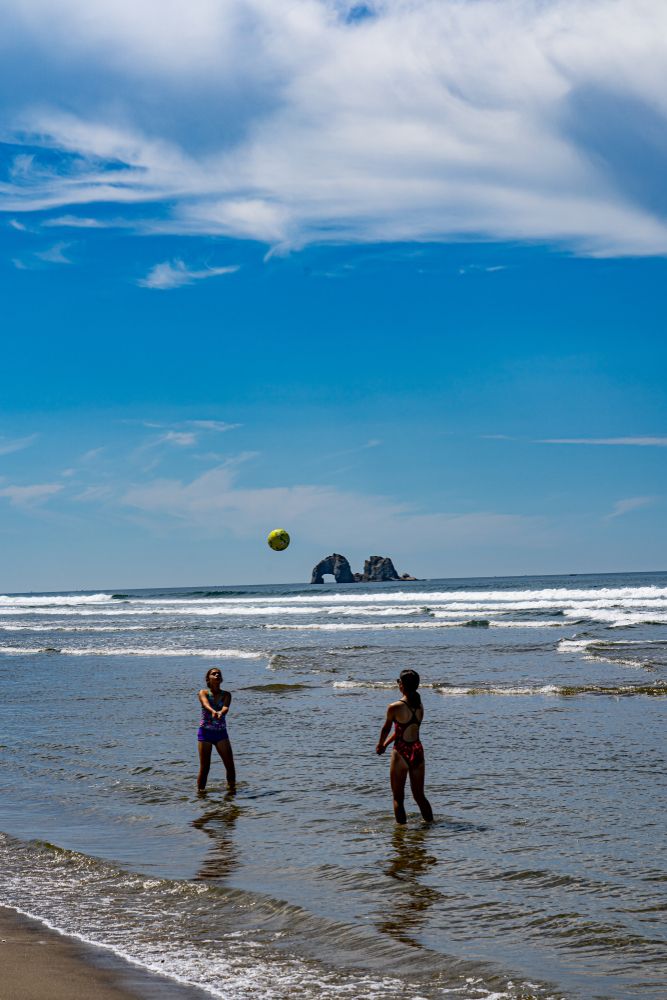 Two people playing volleyball on the beach with the Twin Rocks on the background.