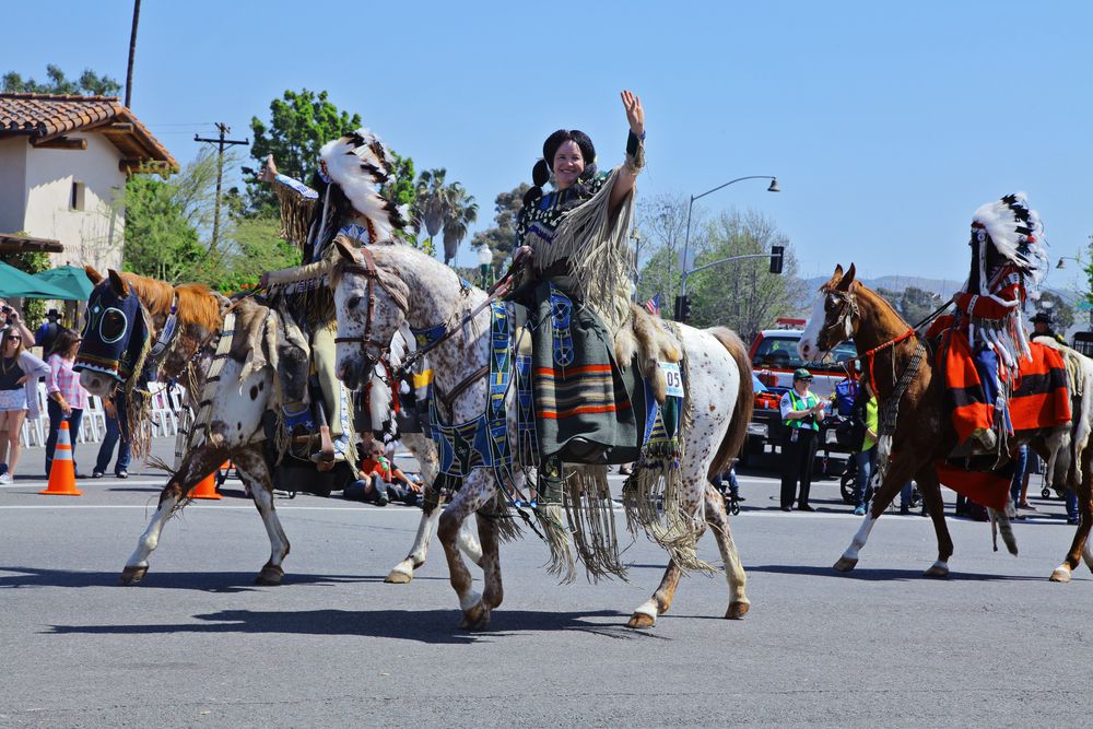 Woman waving while riding a horse at Swallows Day Parade.