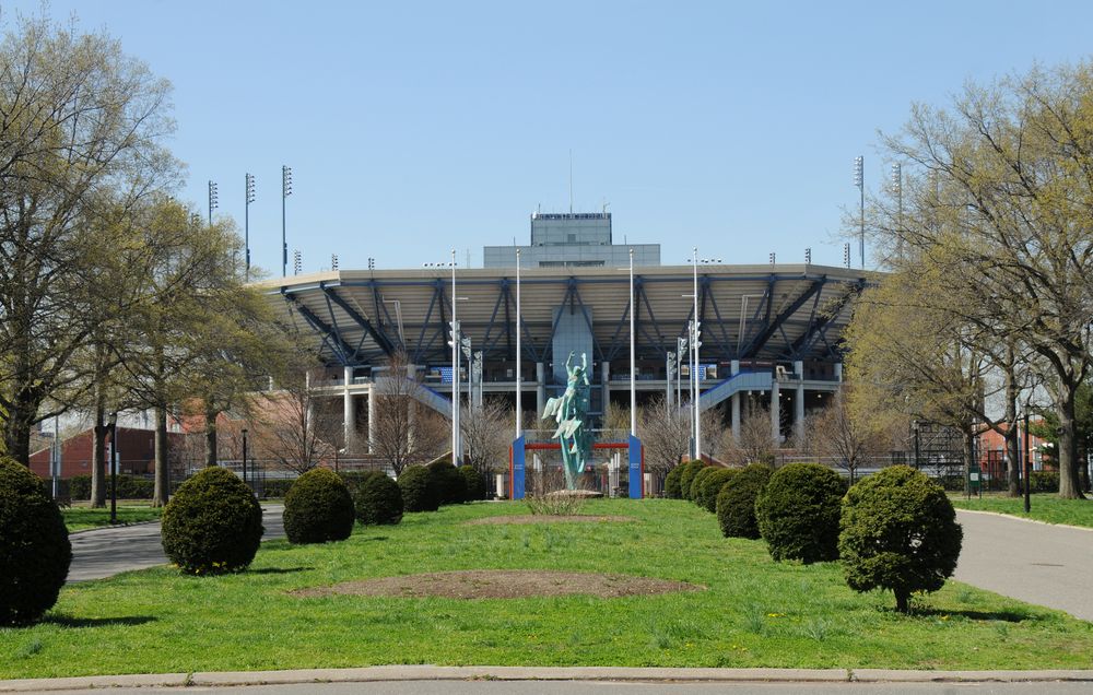 Exterior view of the National Tennis Center, ladscaped with green bushes and grass.