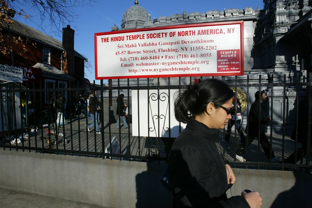 A woman wearing sunglasses passing by the Hindu temple signage.